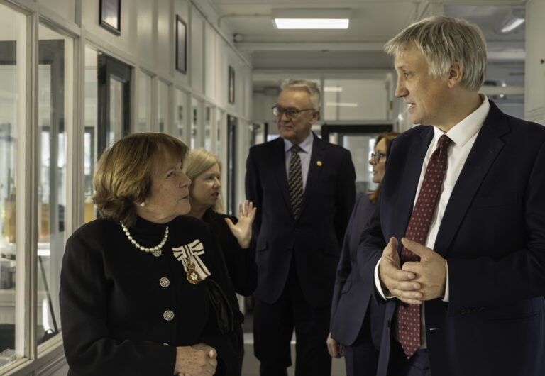 Julius Walters speaking with Lady Clare as they walk down corridor touring the mill, other deputies are in background
