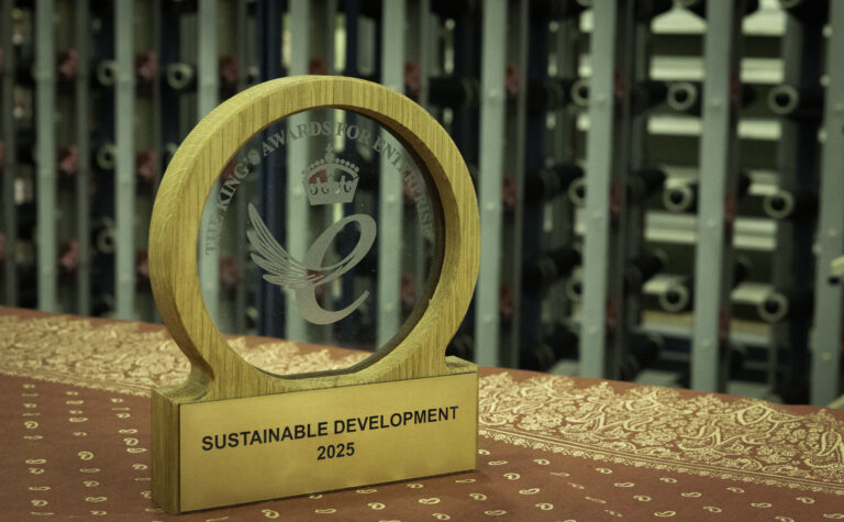 Wooden and glass trophy engraved with King's Award for Enterprise logo on table, with cones of yarn in background on machinery